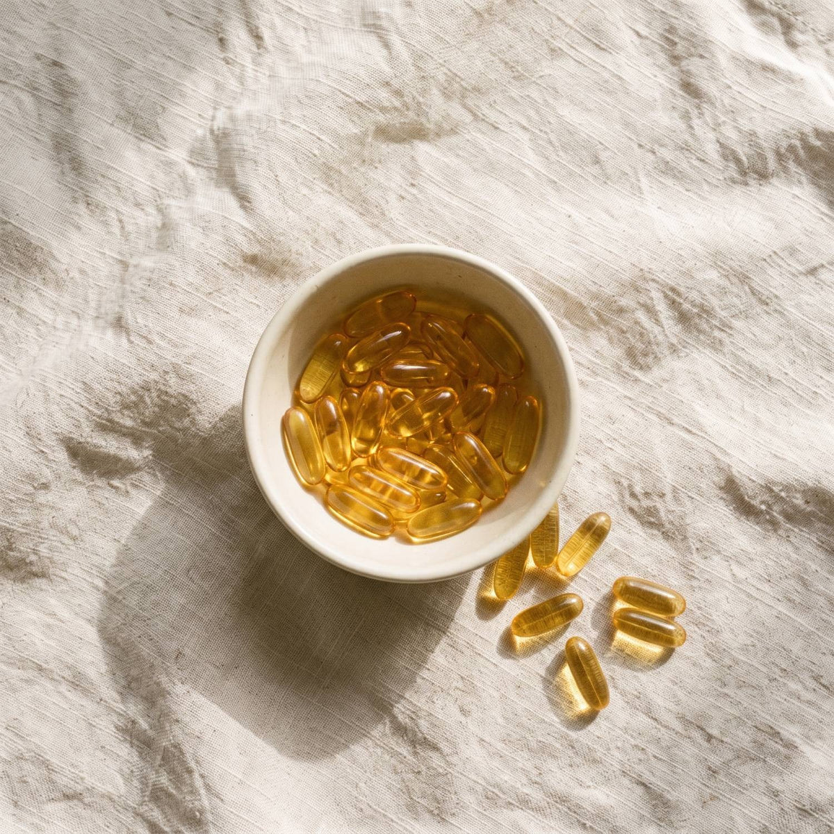 A bowl of golden softgels on linen
